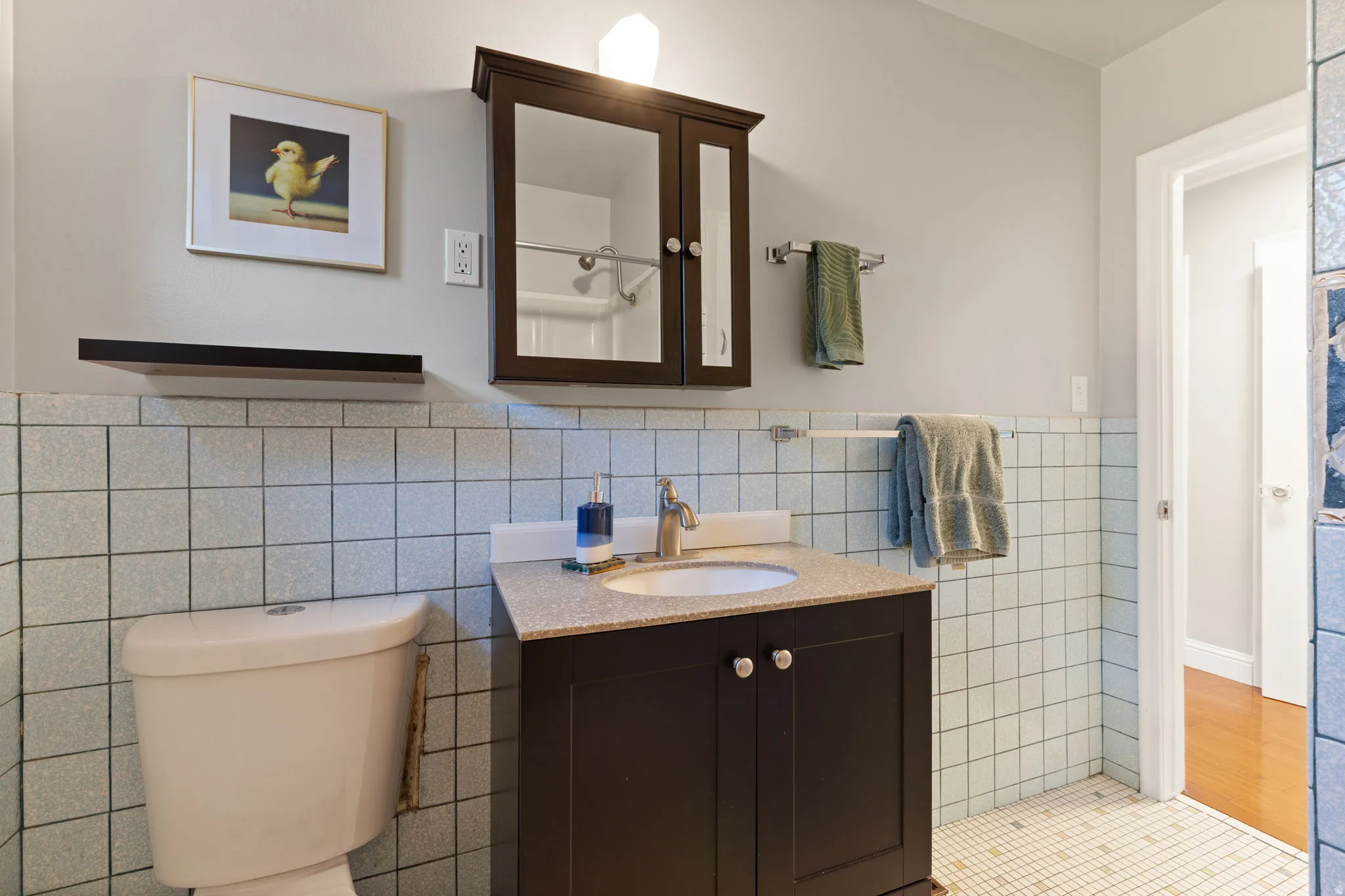 Bathroom with square wall tiling, dark wood-finish vanity, integrated sink, and wall-mounted medicine cabinet