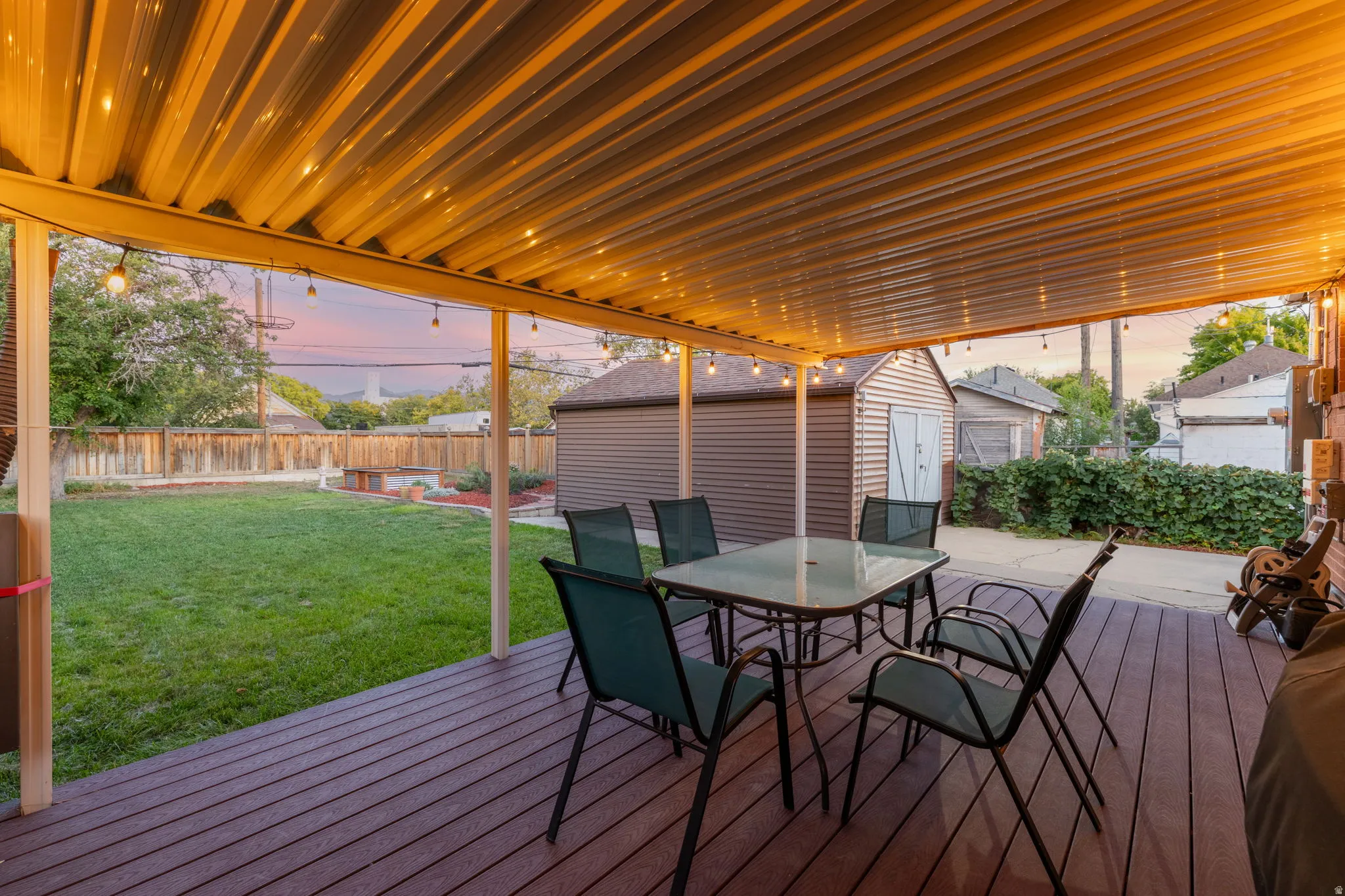 Covered outdoor living space featuring string lighting, wood-finish decking, and a fenced backyard with a detached shed