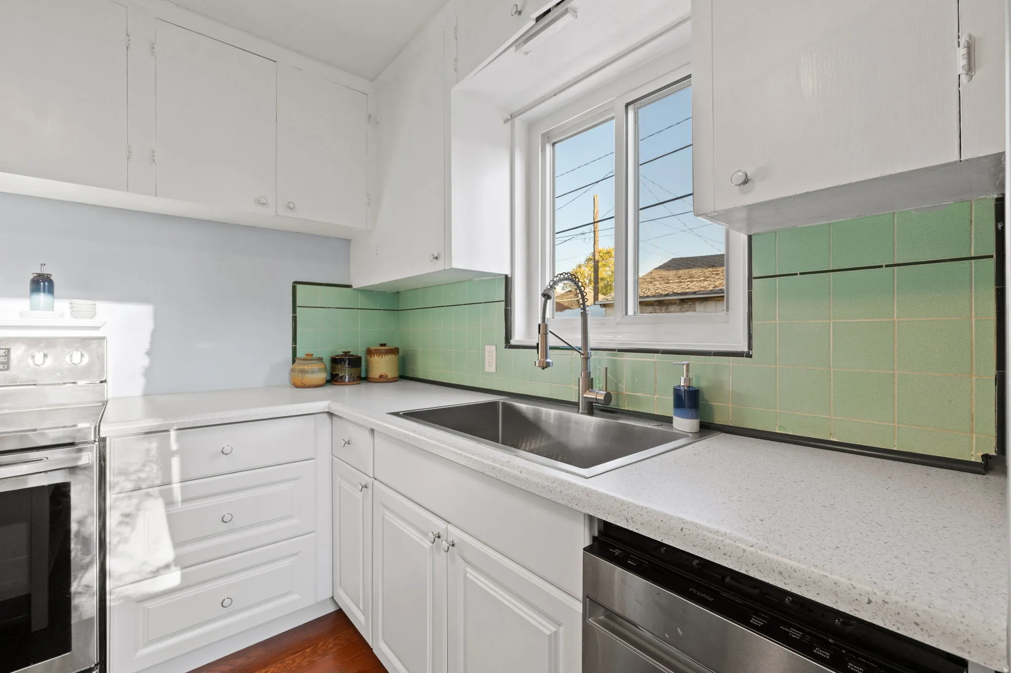 White cabinetry, stainless steel sink with a gooseneck faucet, light-toned countertops, and an integrated dishwasher