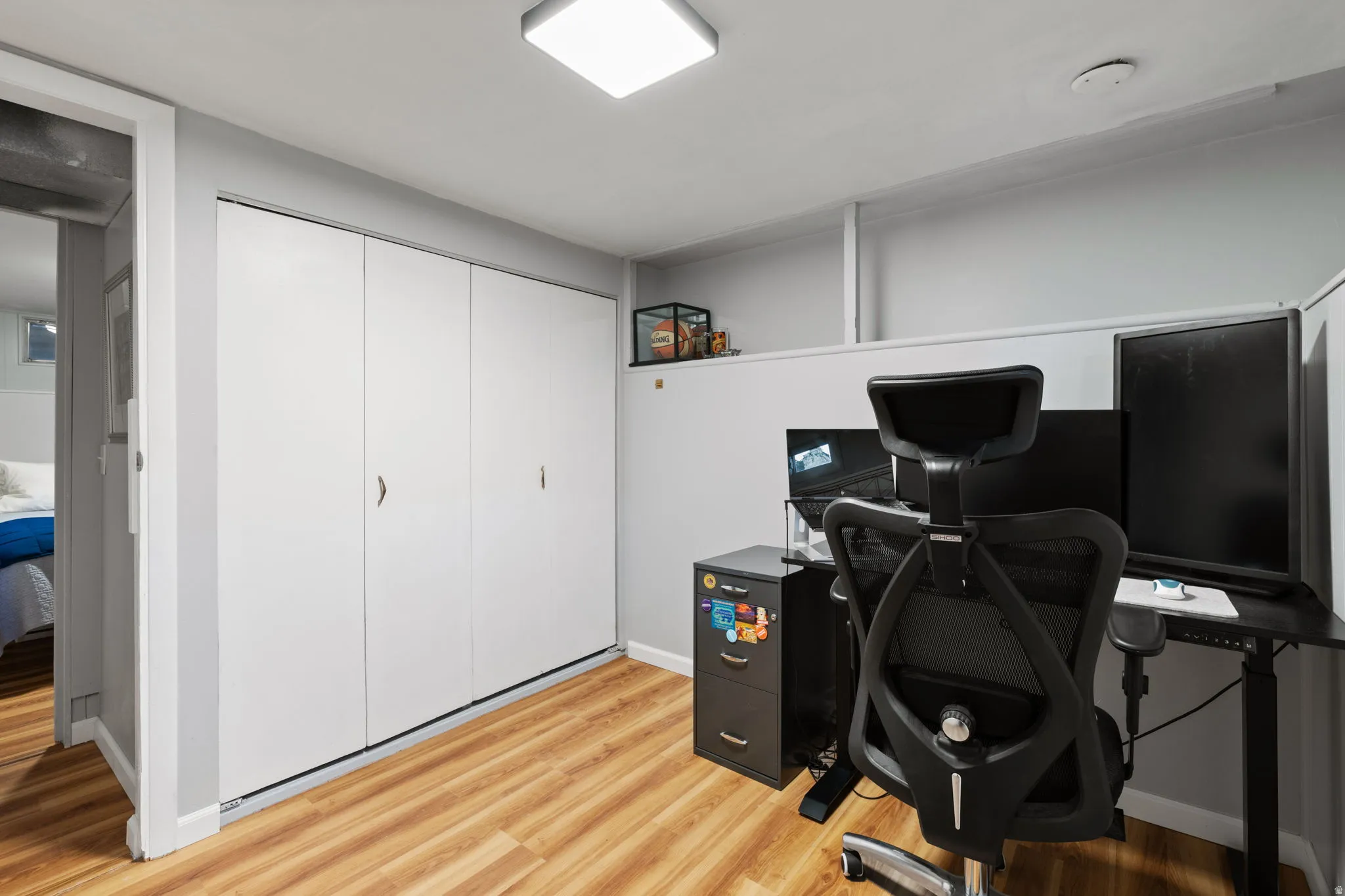 Wood-finish flooring, white bi-fold closet doors, square ceiling light fixture, and a partial wall separation
