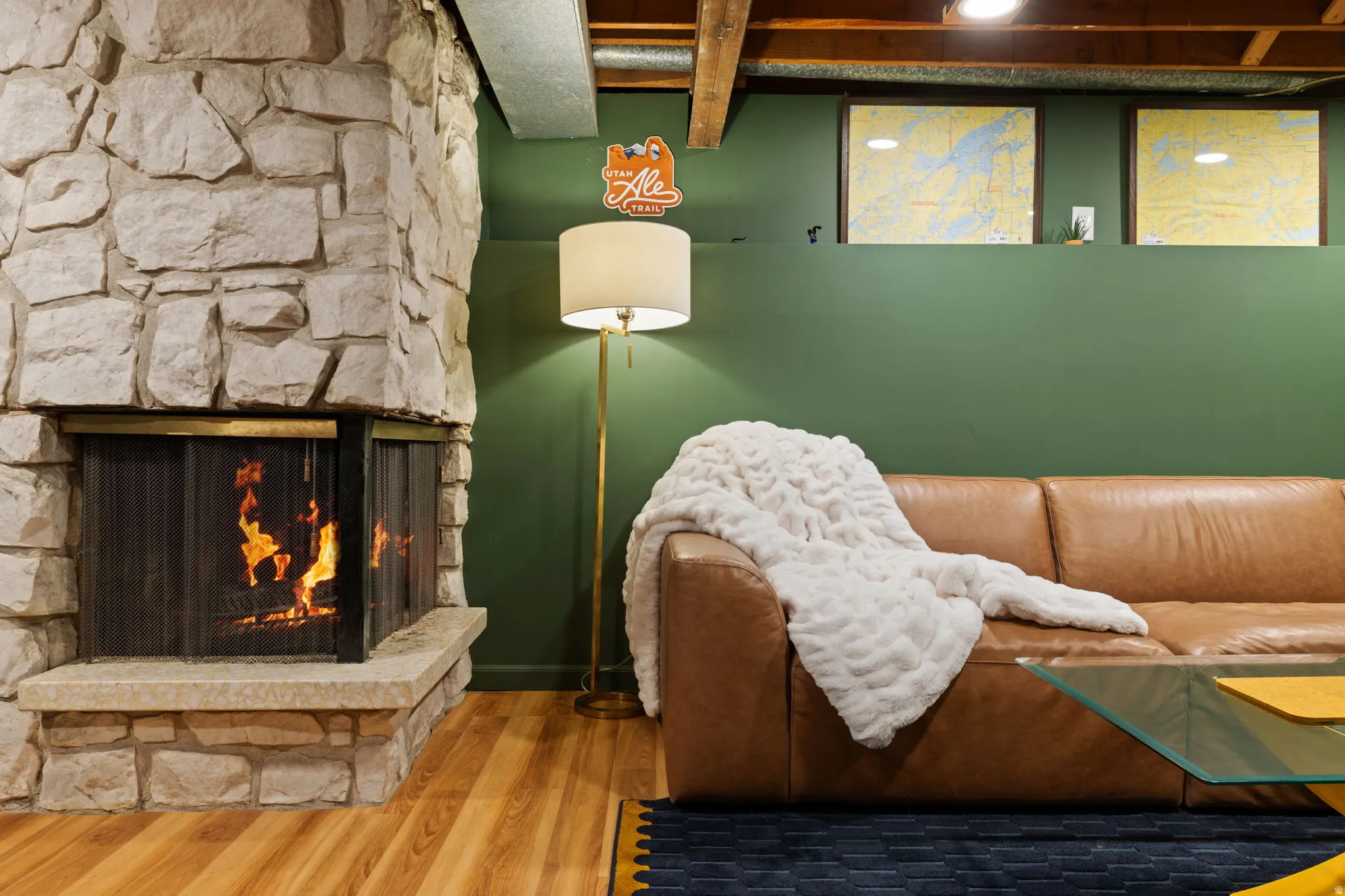 Stone-clad fireplace with hearth, wood-finish flooring, exposed ceiling beams, and painted wall paneling