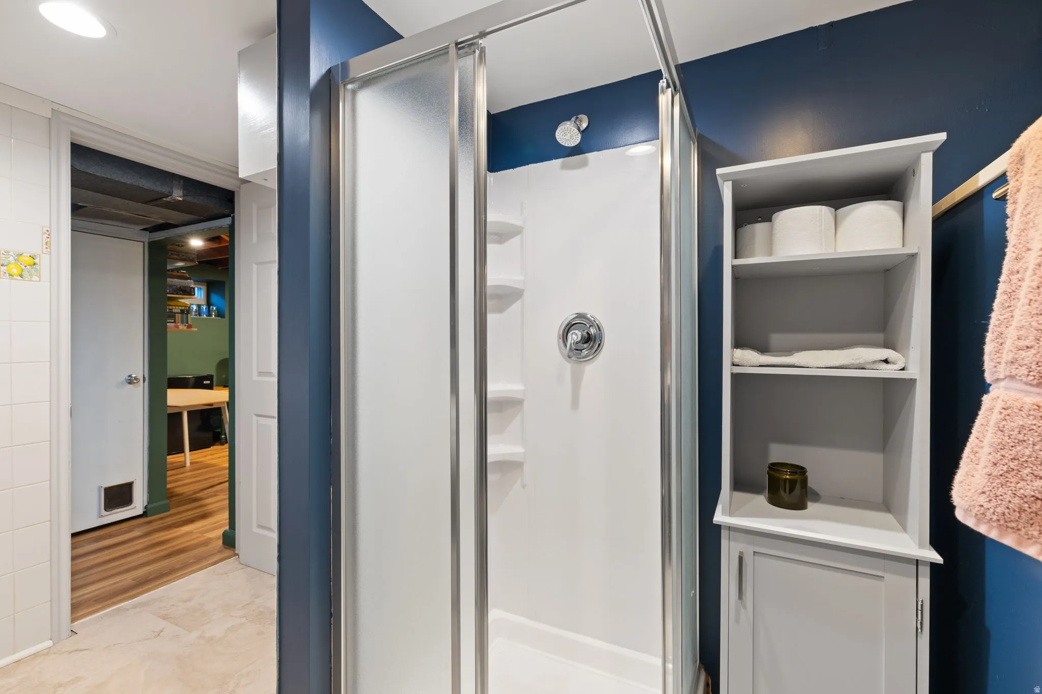 Enclosed shower with sliding glass door, chrome fixtures, and built-in shelving