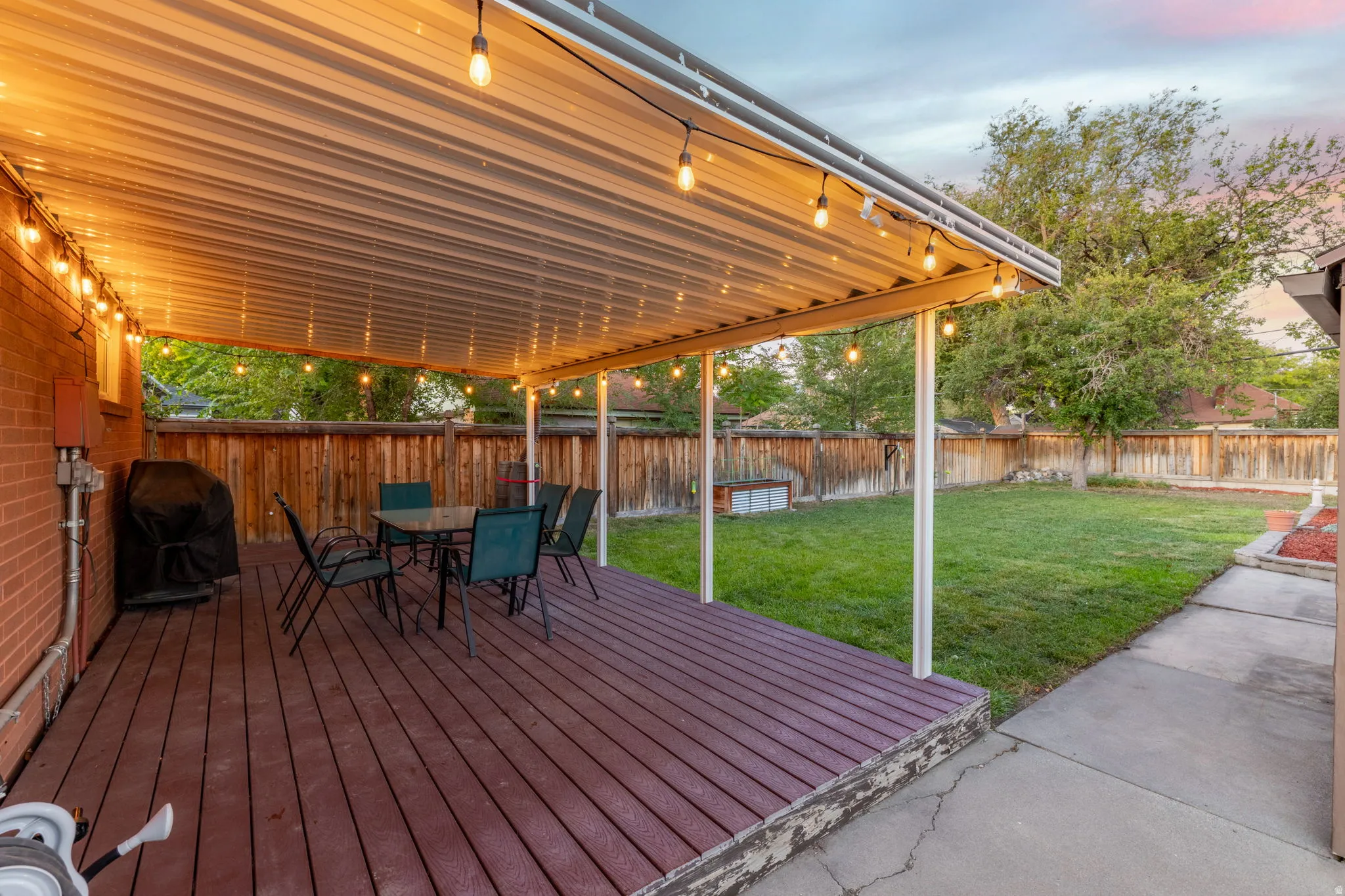 Expansive backyard featuring a covered patio, wood-finish decking, and a manicured lawn