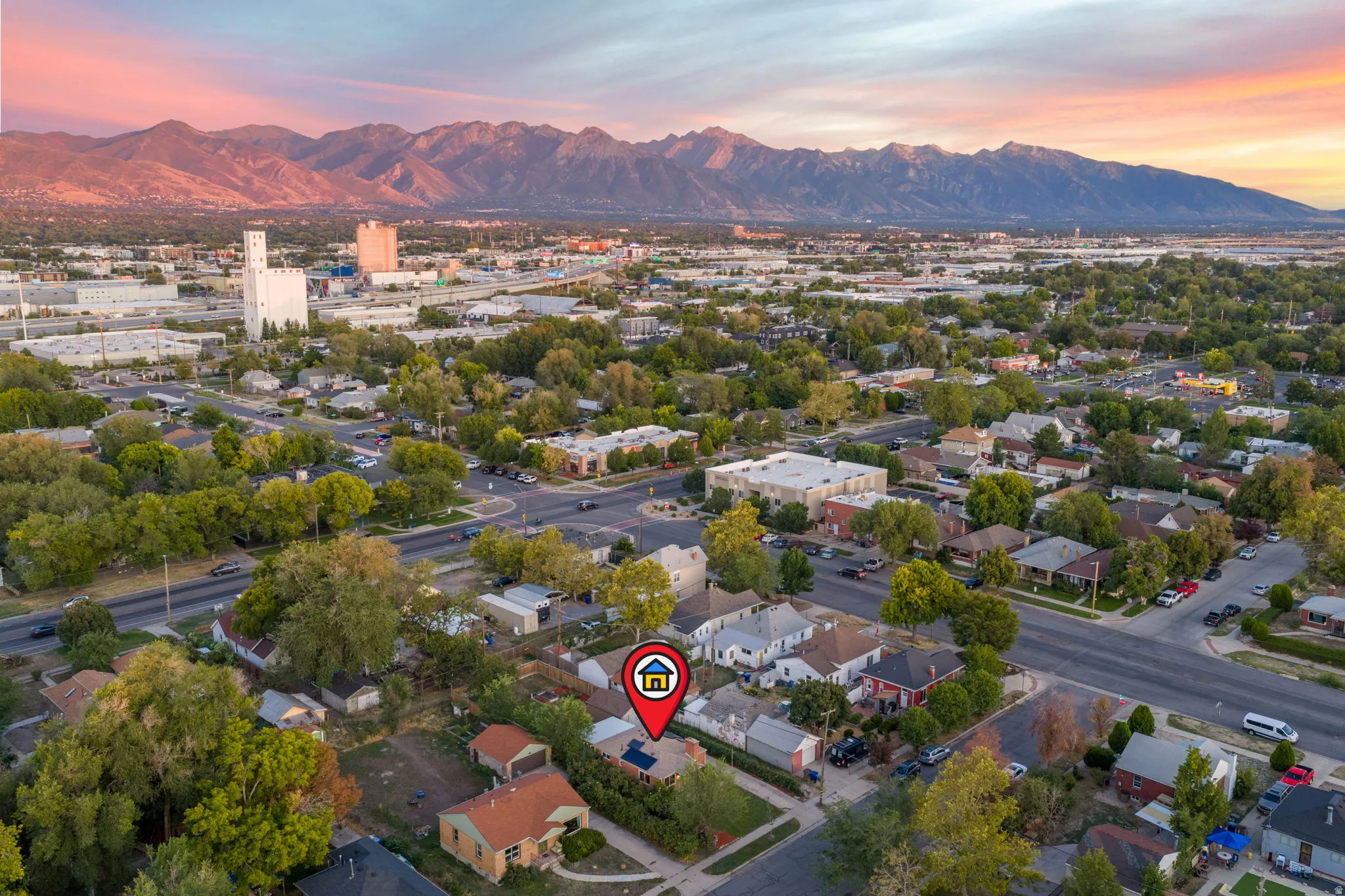 Residential property with solar panels, surrounded by mature trees and paved streets, set against a backdrop of distant mountains and a city skyline
