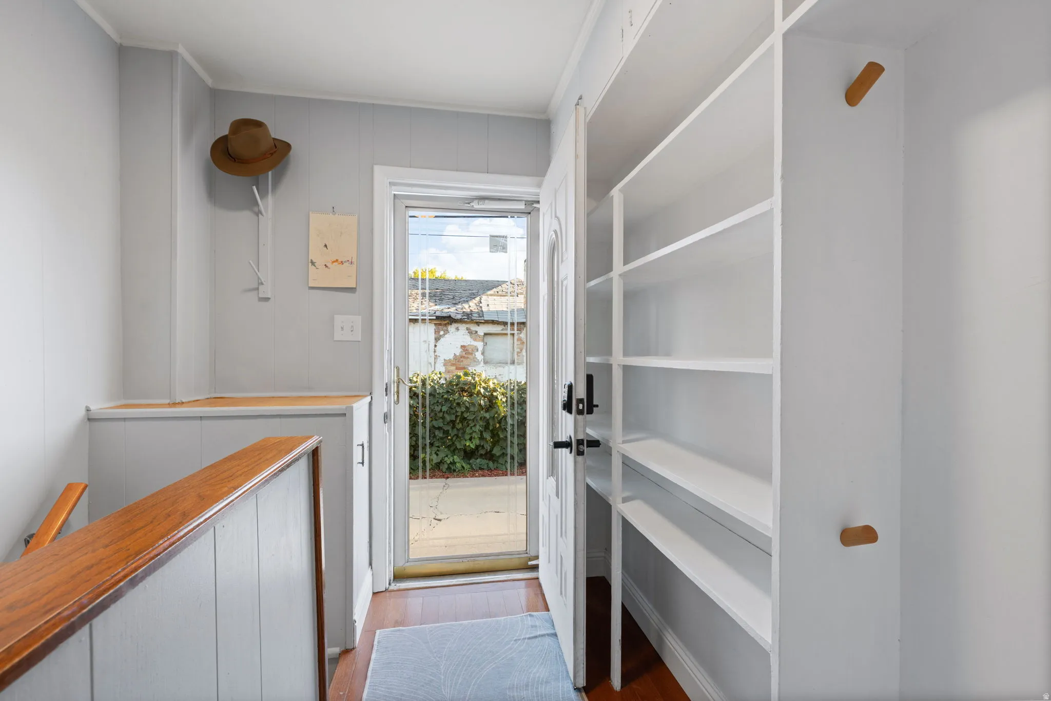 Built-in shelving, wood-finish flooring, half-wall paneling, and a full-light entry door
