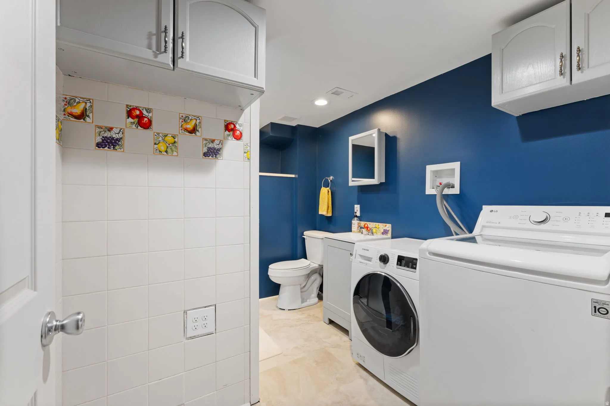 Laundry area featuring tile flooring, white wall tiling with decorative accents, and overhead cabinetry