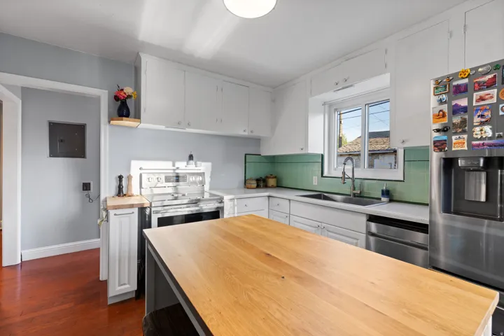Kitchen featuring wood-finish flooring, white cabinetry, stainless steel appliances, a wood-finish island, and a tiled backsplash
