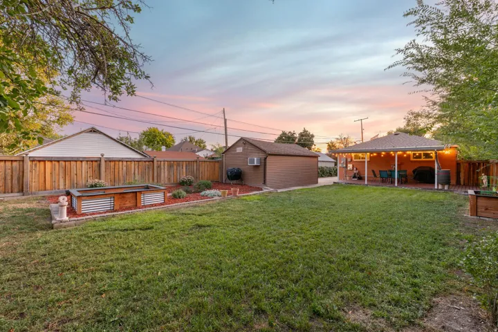 Expansive backyard featuring a covered patio, a detached shed, a full privacy fence, and a raised garden bed