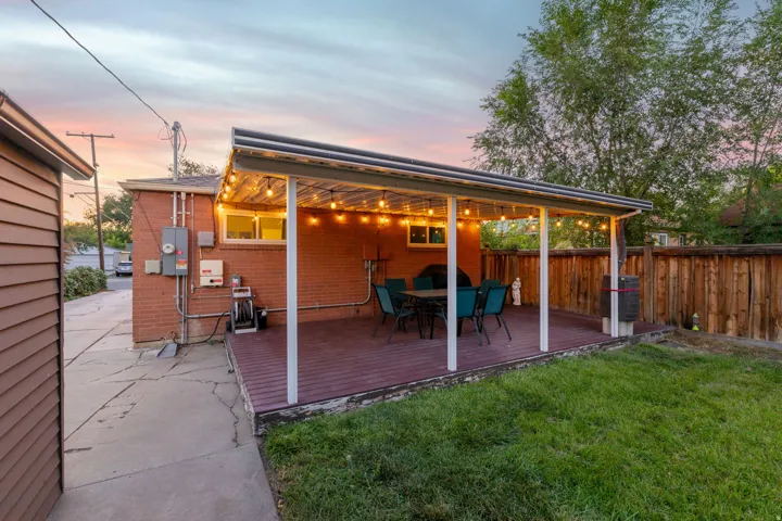 Covered patio with a dark wood-finish deck, brick exterior, and a privacy fence