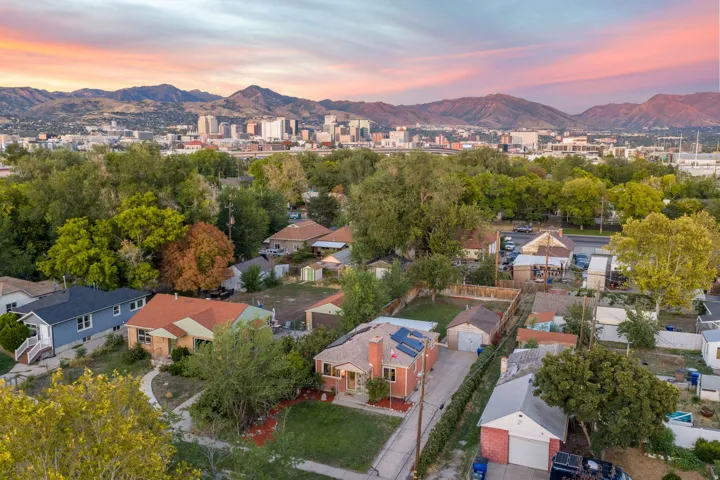 Residential property with a brick exterior, solar panels, mature trees, and a detached garage, set against a mountain and city skyline backdrop