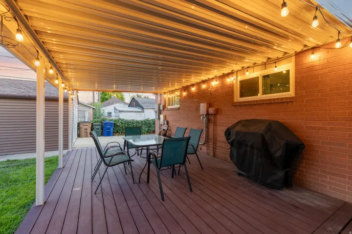Covered outdoor patio with a corrugated roof, wood-finish decking, and brick exterior wall