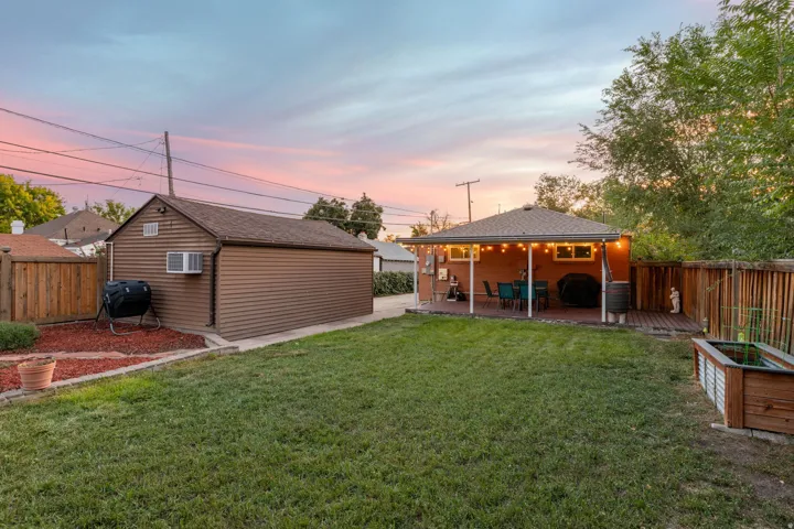 Expansive grassy yard area with a covered patio, wood deck, and detached outbuilding