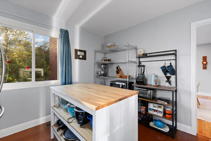 Kitchen area featuring wood-finish flooring, a white-framed window, and a white kitchen island with a butcher block countertop