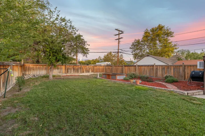 Expansive fenced backyard featuring a manicured lawn, established tree, and a landscaped garden bed with a stone-edged border