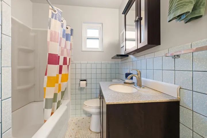 Bathroom featuring a built-in tub with shower, single window, vanity with integrated sink, and wall-mounted storage cabinet
