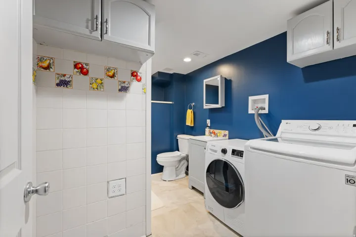 Laundry area featuring tile flooring, white wall tiling with decorative accents, and overhead cabinetry
