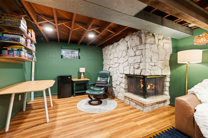 Stone fireplace with a corner hearth, wood-finish flooring, exposed wood beam ceiling, recessed lighting, and built-in shelving