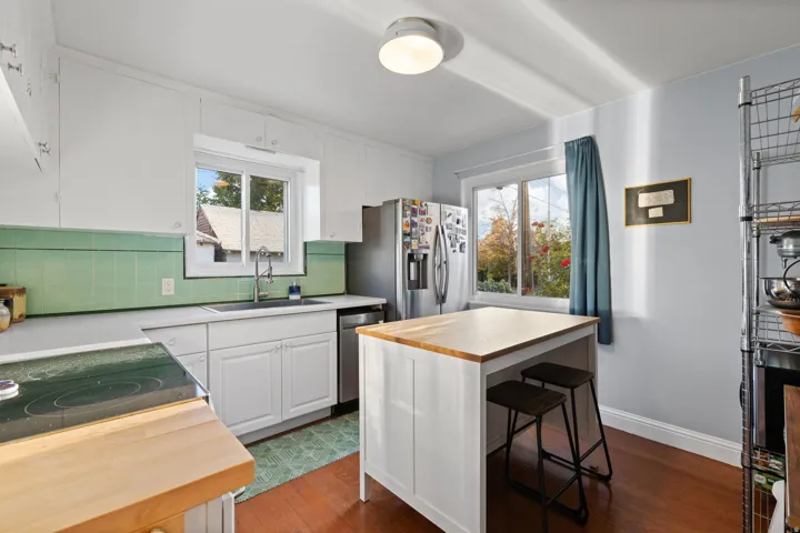 White cabinetry paired with a green tile backsplash, stainless steel refrigerator, and a kitchen island with a wood-finish countertop