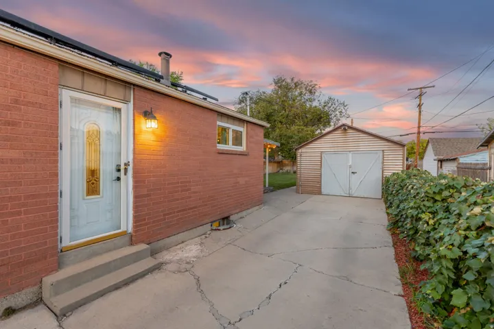 Brick exterior with a white entry door, exterior wall sconce, and a detached garage with double doors