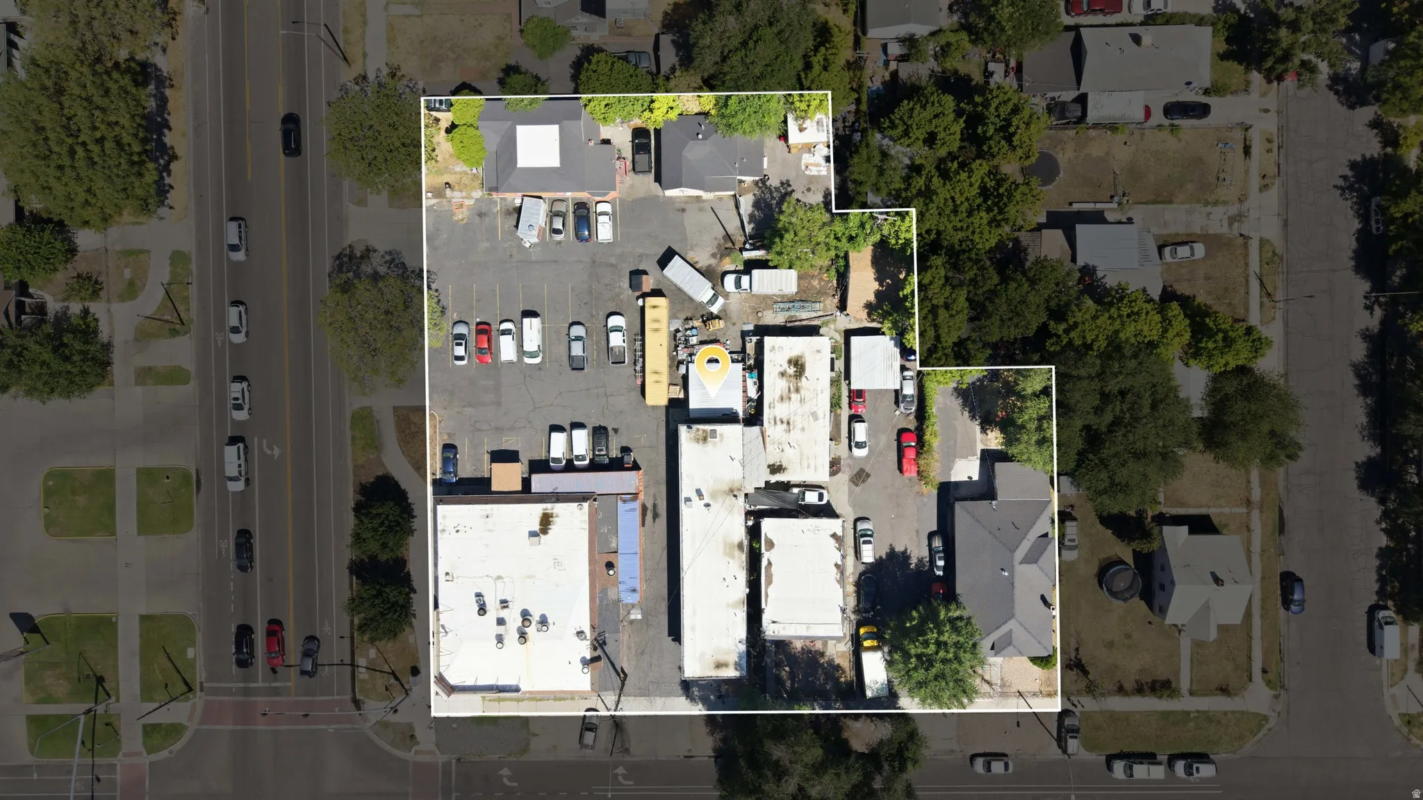 Aerial view of a commercial property featuring multiple buildings, extensive paved parking areas, and mature perimeter trees
