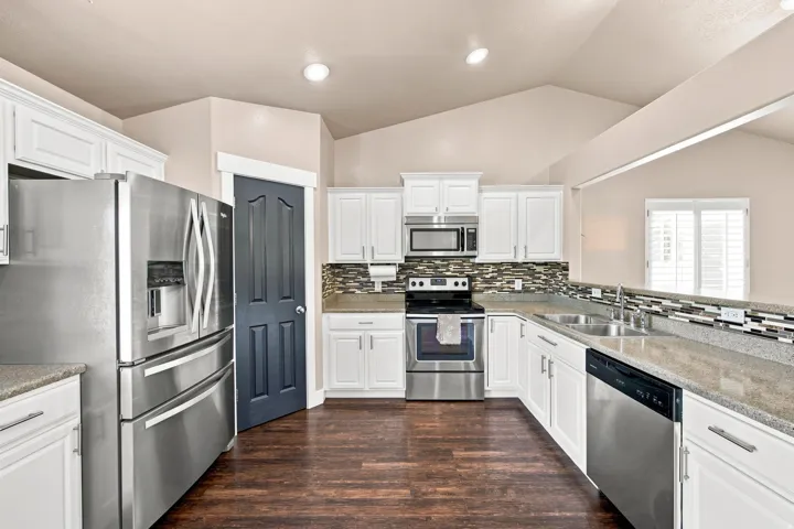 Kitchen featuring white cabinetry, stainless steel appliances, wood-finish flooring, and a tiled backsplash