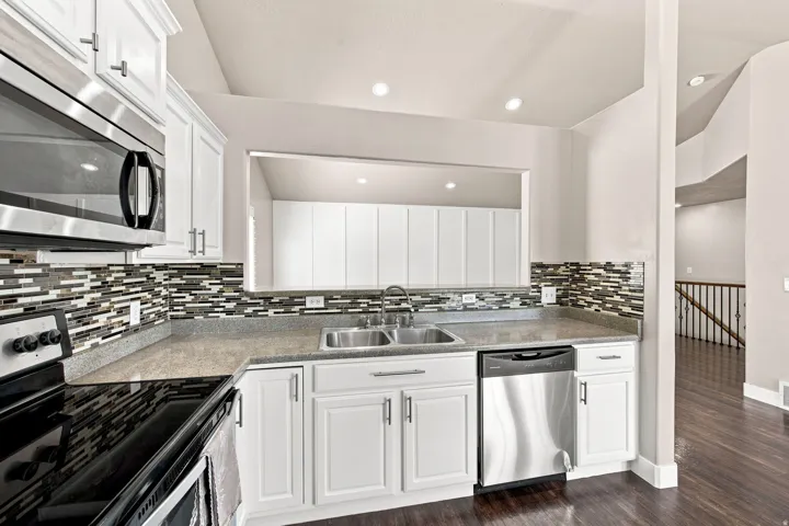 Kitchen featuring white cabinetry, a dual-basin stainless steel sink, stainless steel appliances, a mosaic tile backsplash, and recessed lighting