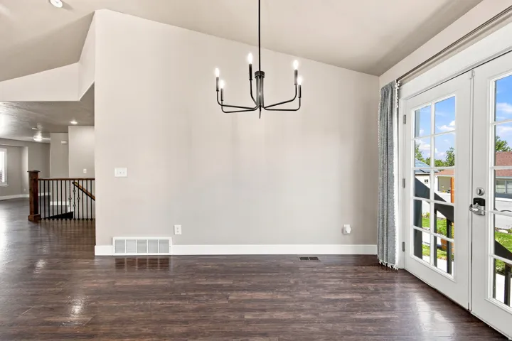 Wood-finish flooring, vaulted ceiling, contemporary chandelier, crisp white trim, and a double French door