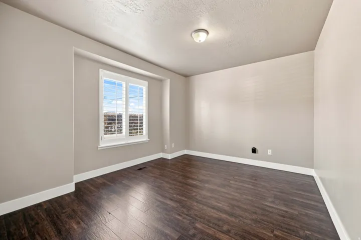 Rich wood-finish flooring, white trim, neutral wall paint, recessed window with white shutters, and a ceiling-mounted light fixture