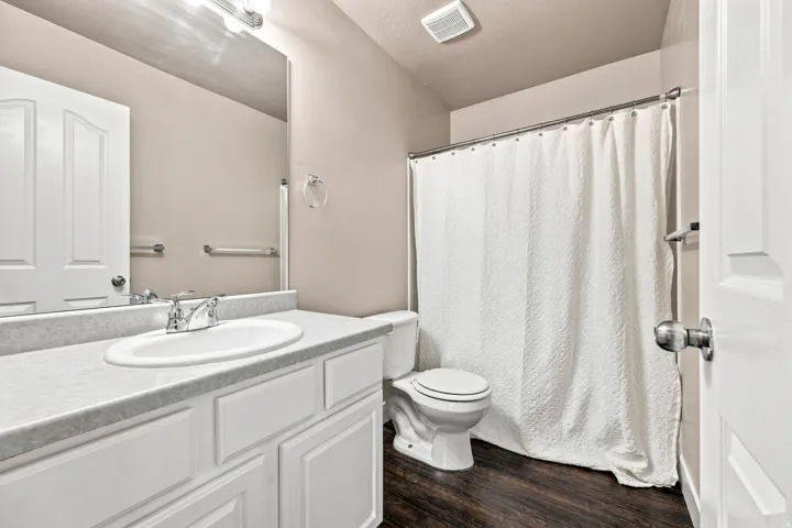 Recessed lighting over vanity, wood-finish flooring, and white paneled cabinetry with chrome hardware