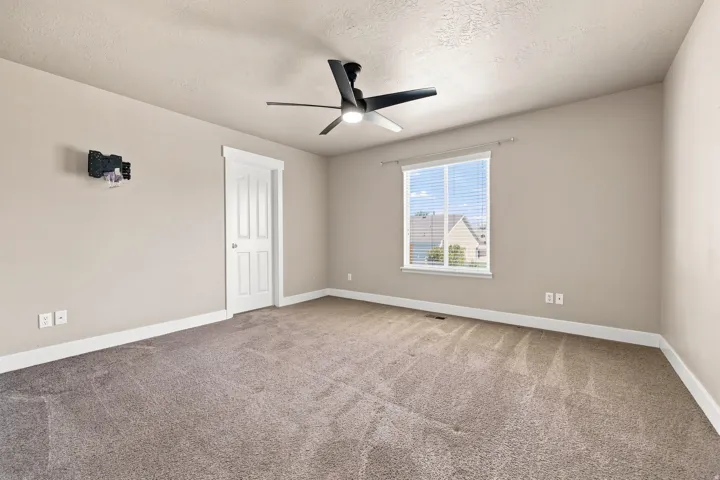 Primary. Neutral tone walls, plush carpeting, white trim, recessed window with blinds, and a modern ceiling fan