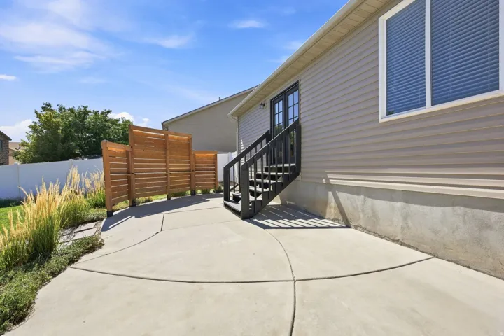 Concrete patio, wood privacy screen, exterior siding, dark-stained wood stairs, and double-pane window