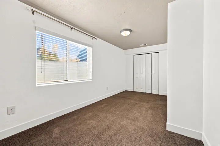 Bed 5. Neutral wall paint, plush carpet flooring, louvered window blinds, flush-mount ceiling fixture, and bi-fold closet doors
