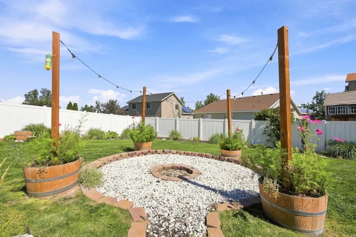 Expansive yard featuring a gravel fire pit area with a brick border, string lights, and wooden barrel planters