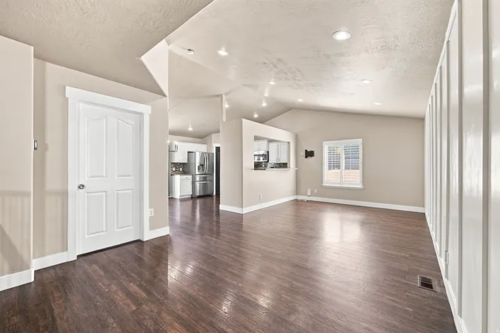 Vaulted ceilings, recessed lighting, wood-finish flooring, white paneled accent wall, and a pass-through window to the kitchen