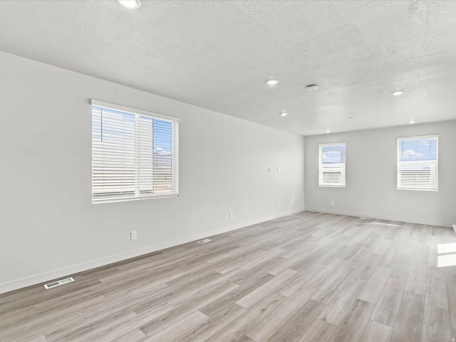 Spacious room featuring multiple windows, recessed lighting, and wood-finish flooring