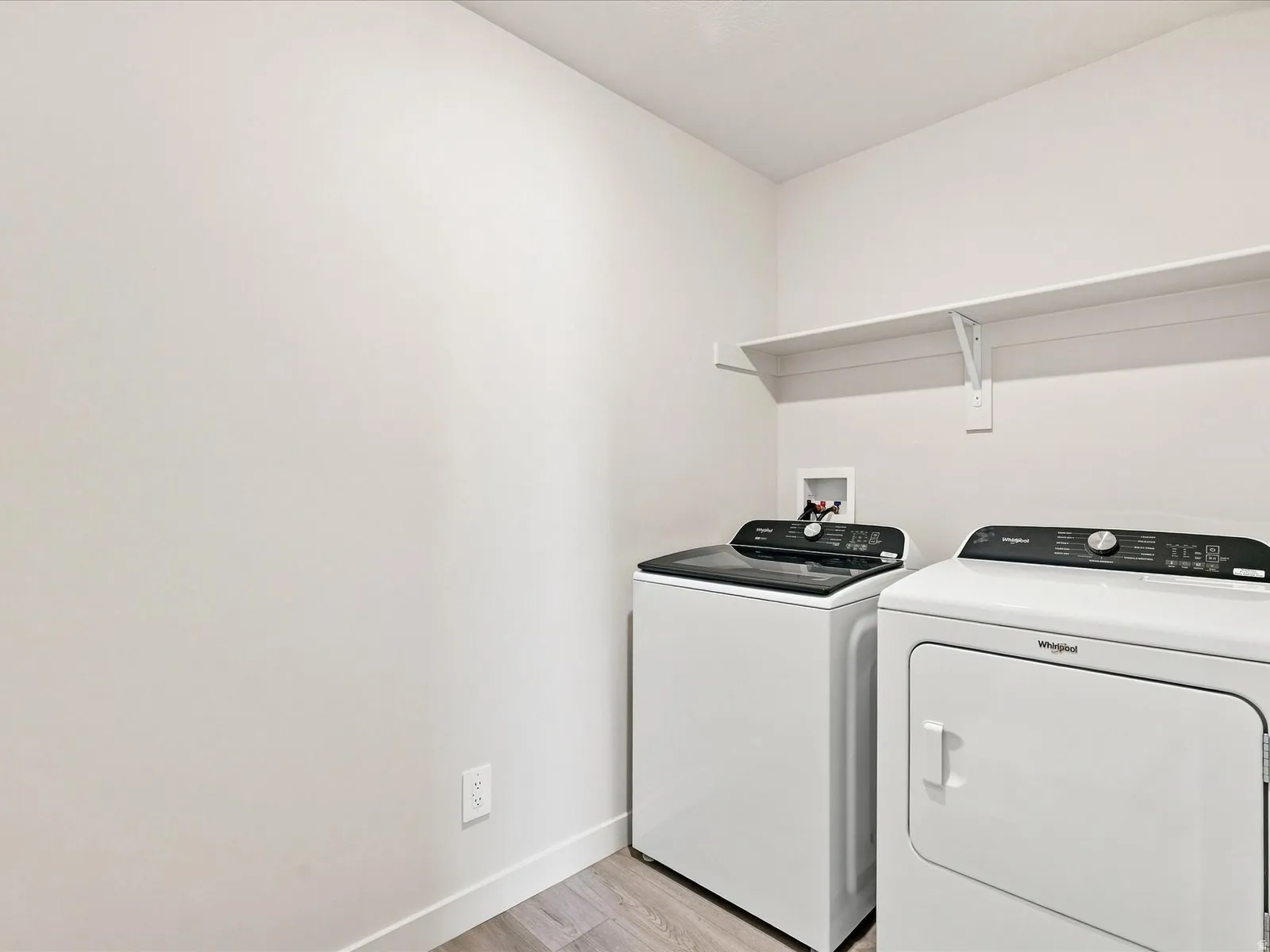 Dedicated laundry space with wood-finish flooring and integrated shelving