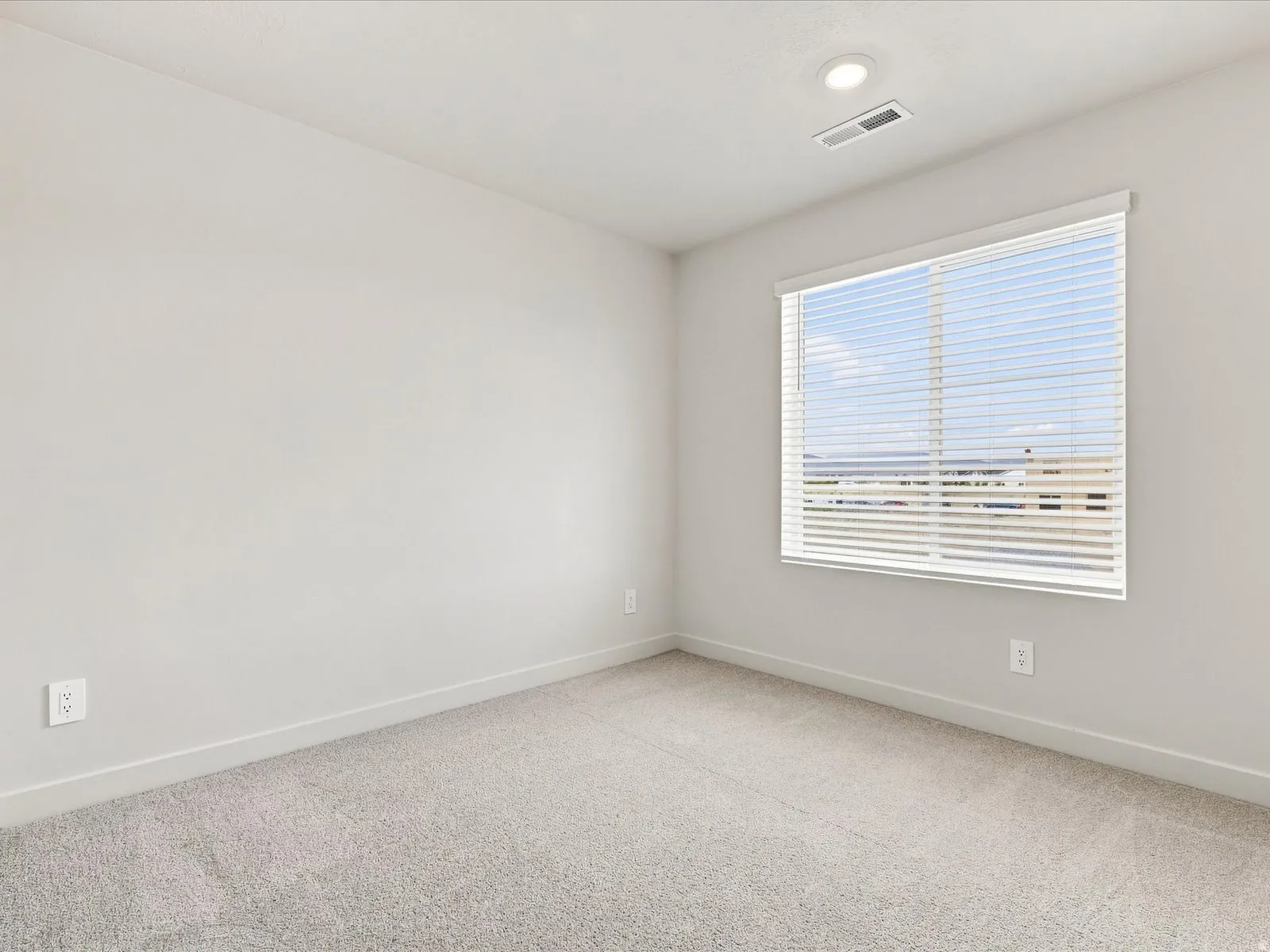 Recessed ceiling lighting, light gray wall paint, window with blinds, light gray carpeting