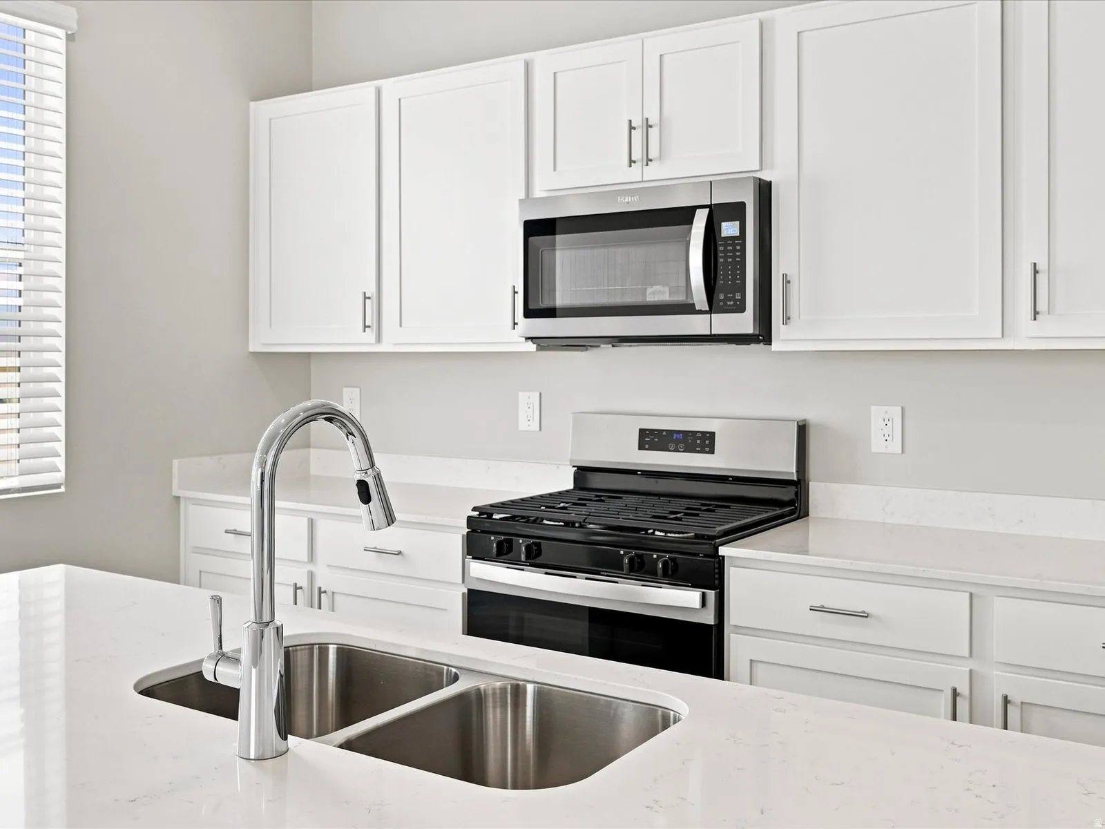Kitchen featuring white cabinetry, light-toned countertops, a stainless steel gas range, and an over-the-range microwave