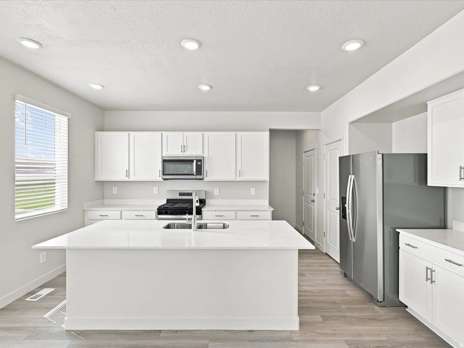 White kitchen featuring a center island, recessed lighting, white cabinetry, a stainless steel refrigerator, and wood-finish flooring