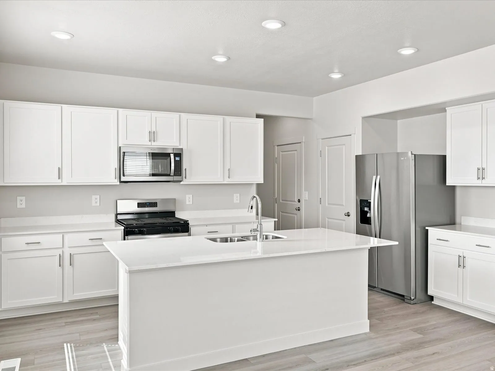 Kitchen featuring stainless steel appliances, white cabinetry, a center island with sink, light-colored countertops, and recessed lighting