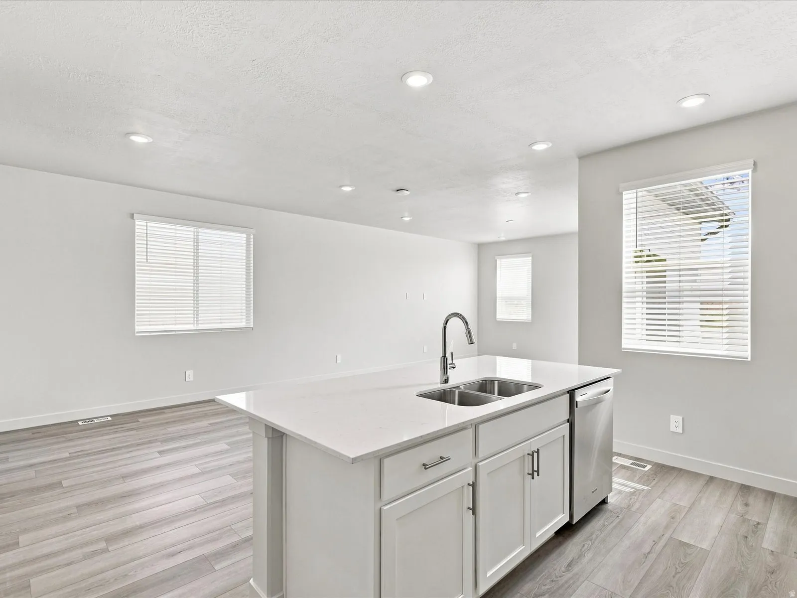 Kitchen island with integrated double basin sink, stainless steel dishwasher, white cabinetry with silver-tone hardware, white countertop, and wood-finish flooring