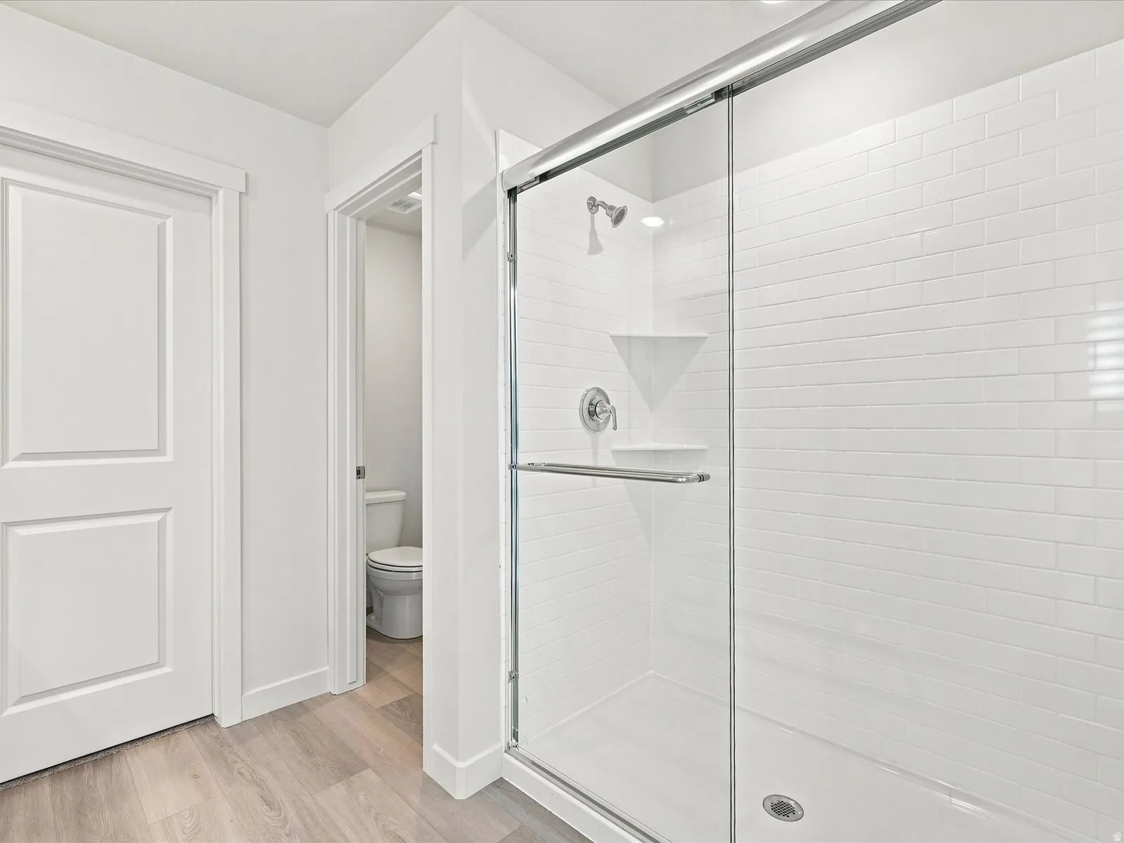 Shower with clear glass enclosure, subway tile surround, corner shelf, recessed lighting, and a chrome shower head