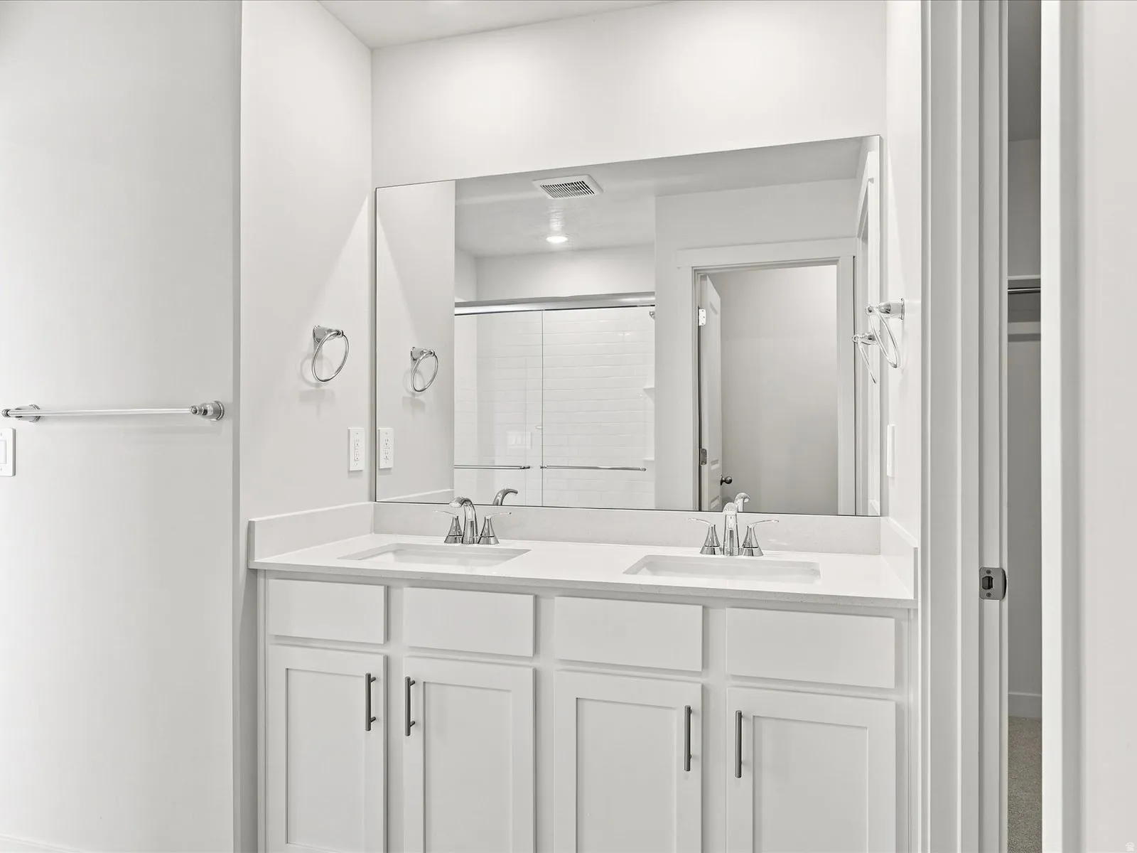 Dual vanity with white cabinetry, polished chrome fixtures, and a large wall-mounted mirror