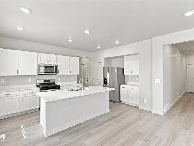 Kitchen featuring white cabinetry, stainless steel appliances, a center island with a sink, and wood-finish flooring
