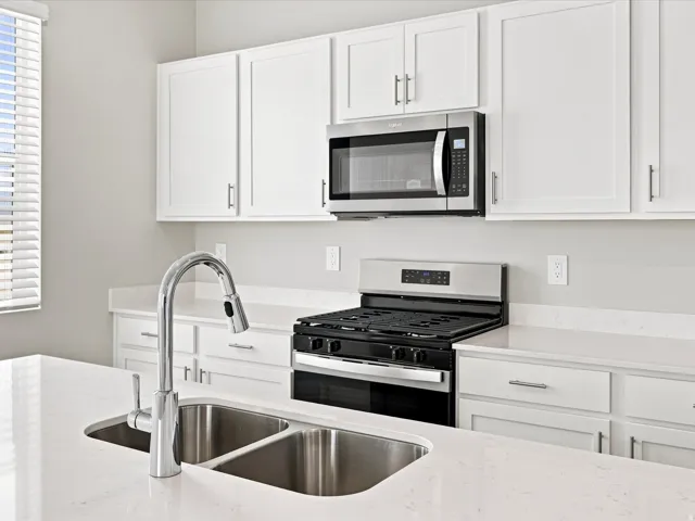 Kitchen featuring white cabinetry, light-toned countertops, a stainless steel gas range, and an over-the-range microwave