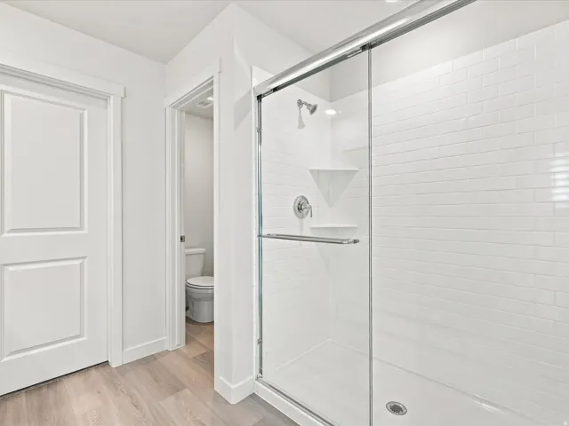 Shower with clear glass enclosure, subway tile surround, corner shelf, recessed lighting, and a chrome shower head