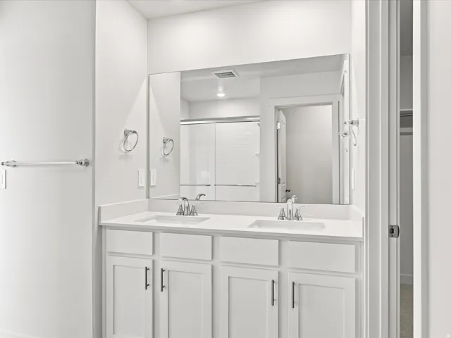 Dual vanity with white cabinetry, polished chrome fixtures, and a large wall-mounted mirror