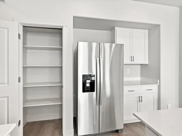 Stainless steel side-by-side refrigerator, white cabinetry with silver-tone hardware, light-toned countertops, and wood-finish flooring