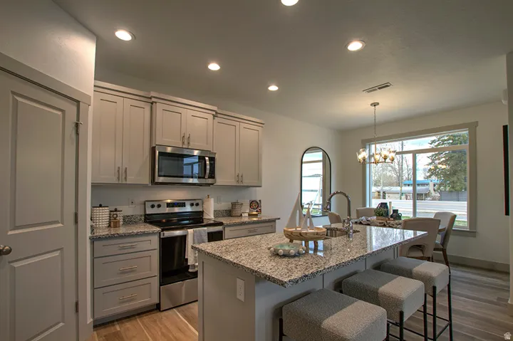 Kitchen featuring granite countertops, stainless steel appliances, light wood-finish flooring, recessed lighting, and a kitchen island with sink