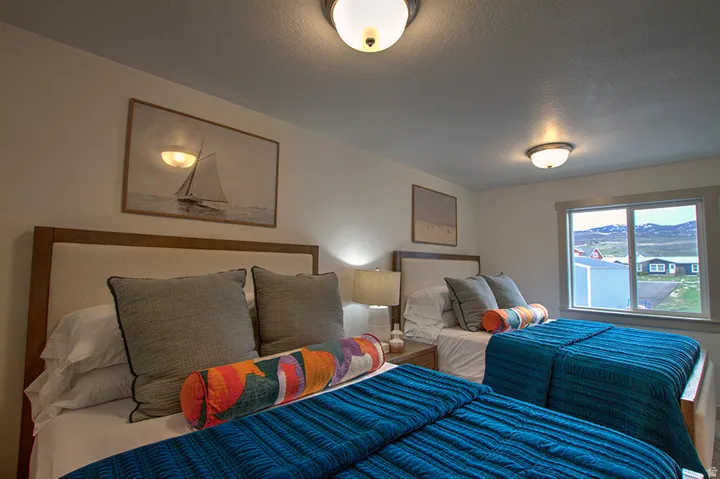 Two beds with upholstered headboards, a bedside table with a lamp, and a window with a mountain backdrop